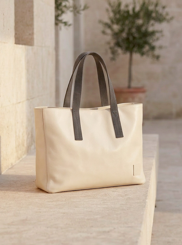 AI-generated hero product shot of a cream leather tote bag resting on a limestone step in a sunlit Mediterranean courtyard, soft golden hour light